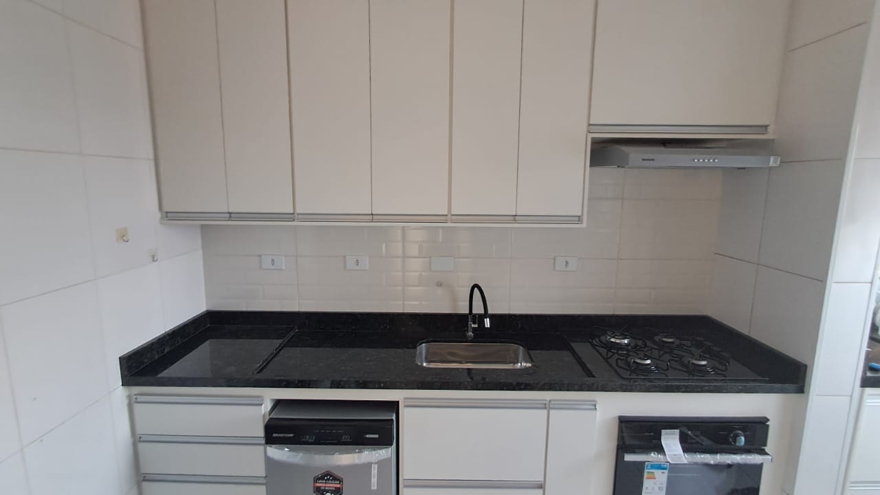 Cozinha planejada sob medida com armários superiores brancos, bancada em granito preto e cooktop.